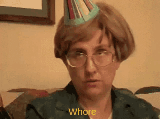 a woman wearing glasses and a party hat is sitting on a couch and saying whore
