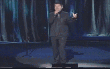 a man in a suit is singing into a microphone on a stage