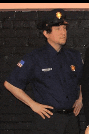 a police officer stands with his hands on his hips in front of a black brick wall