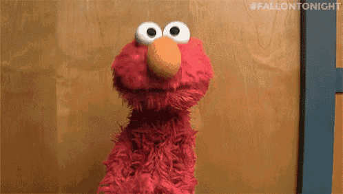 elmo the sesame street character is standing in front of a wooden wall .