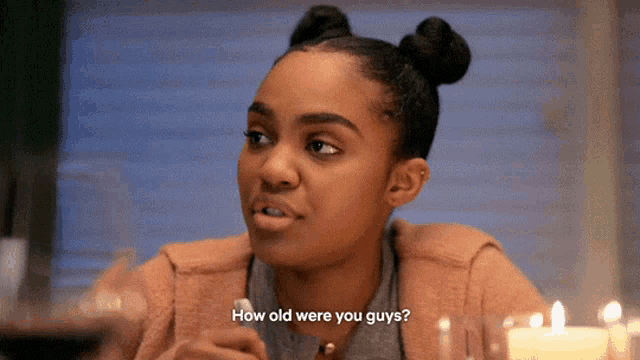 a young woman is sitting at a table with candles and asking how old were you guys
