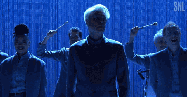 a man in a suit stands in front of a blue curtain with the letters snl on it