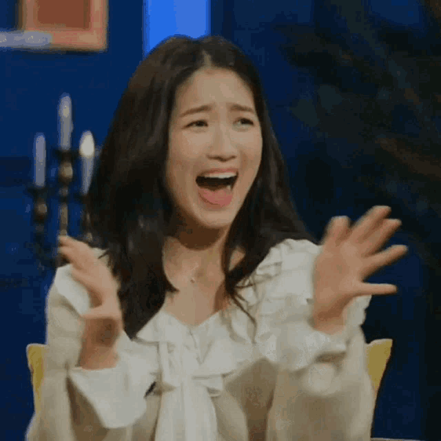 a woman in a white shirt is sitting in a chair with her mouth open and her hands in the air .