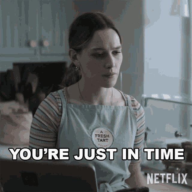 a woman wearing a fresh tart apron is sitting in front of a laptop and says you 're just in time