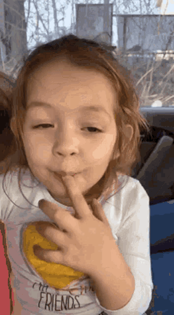 a little girl wearing a shirt that says friends holds her finger to her mouth