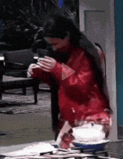 a woman in a red jacket is standing in front of a mirror holding a cup of coffee .