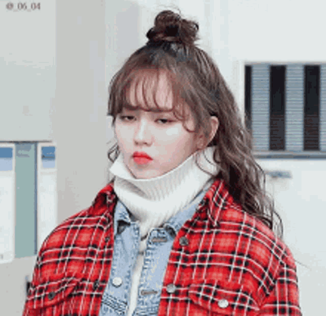 a woman wearing a plaid shirt and a turtleneck is looking at the camera .