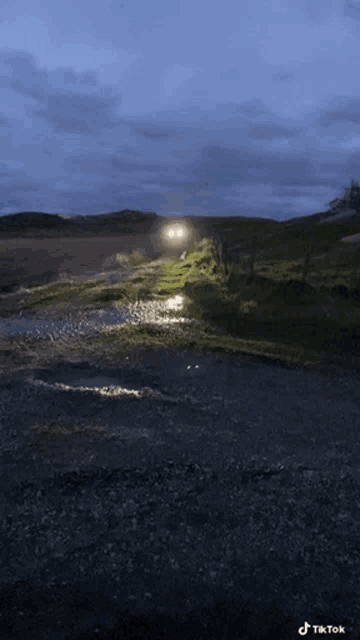 a car is driving down a dirt road with a puddle in the middle