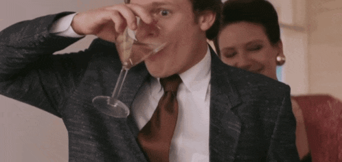 a man in a suit and tie drinks from a glass