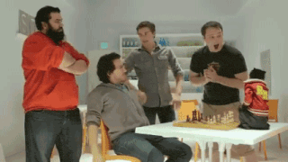 a group of men standing around a table with a chess board on it