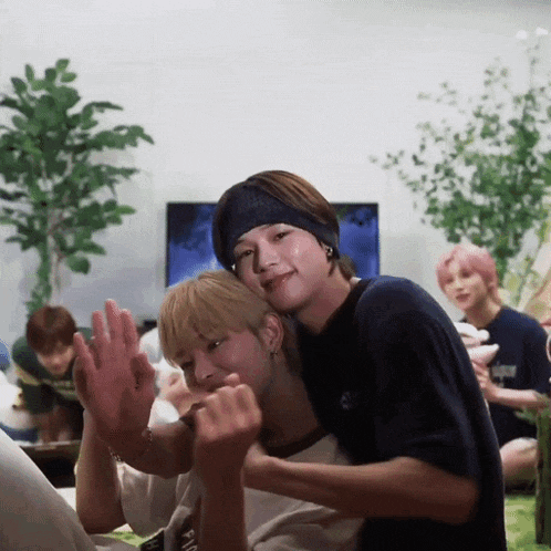 two young men are hugging each other in a living room . one of the men is wearing a headband .