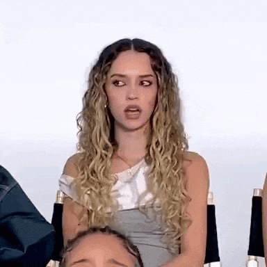a woman with curly hair is sitting in a chair and making a face .