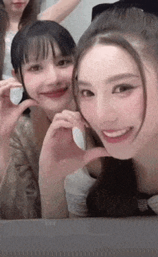 two girls are posing for a picture and one is making a heart shape with her hand .