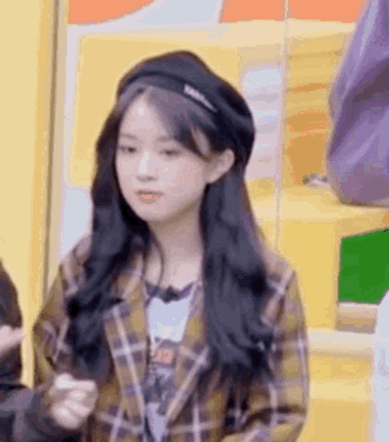 a young woman wearing a plaid jacket and a black beret is standing in front of a yellow wall .