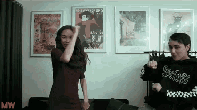a man and a woman are dancing in front of a wall with posters on it including one that says aristide brilant
