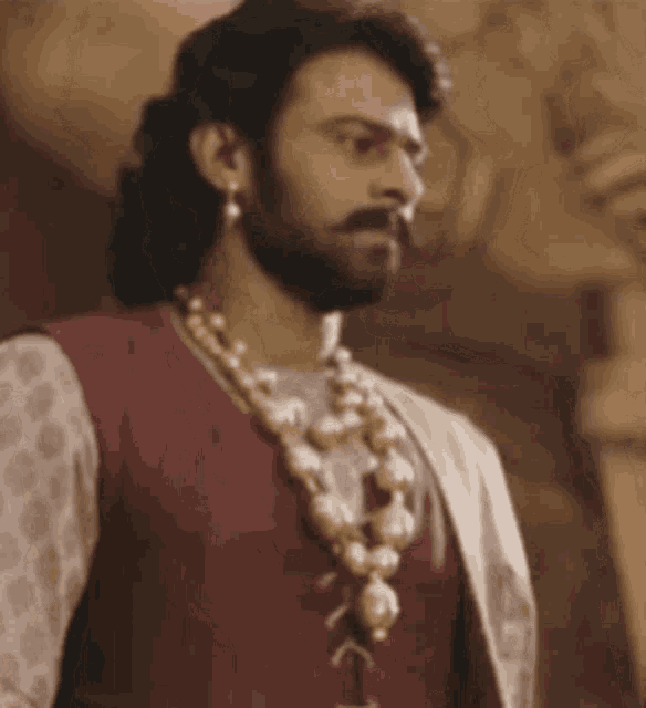 a man with a beard and a pearl necklace is wearing a red vest and a white shirt .