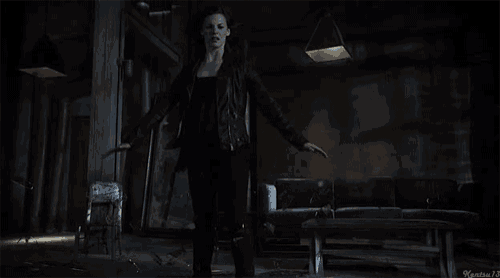 a woman in a black leather jacket is standing in a dark room with her arms outstretched .