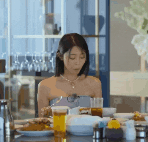 a woman is sitting at a table with plates of food and a glass of orange juice