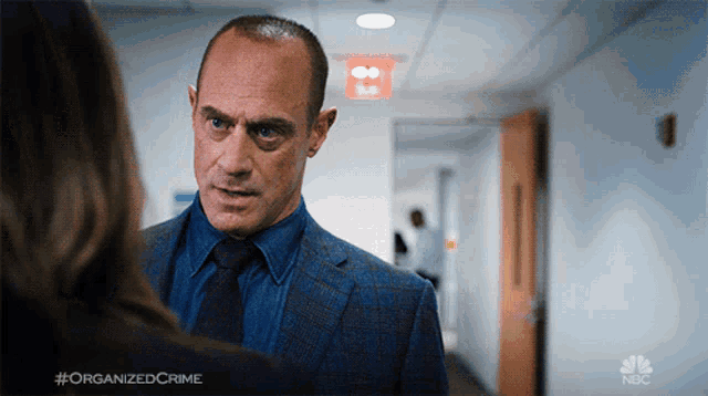 a man in a suit and tie is talking to a woman in a hallway with #organizedcrime written below him