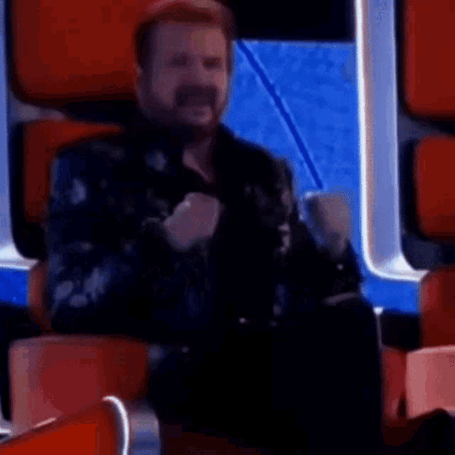 a man with a beard is sitting in a chair with his arms in the air and his fist in the air .