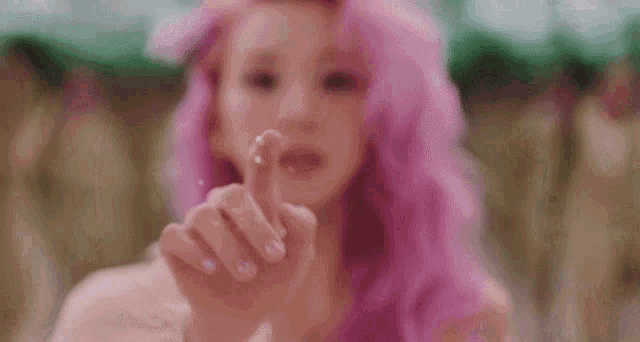 a woman with pink hair is making a heart shape with her hands .