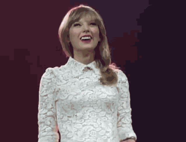 taylor swift is wearing a white lace dress and smiling on a stage .