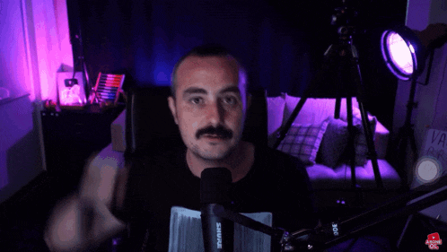 a man with a mustache stands in front of a shure microphone in a dark room