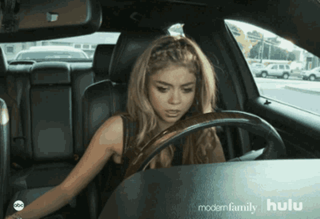a woman is driving a car with a hulu logo on the dashboard