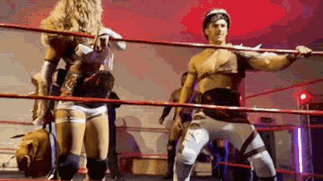 a man and a woman are standing in a wrestling ring holding a sword .