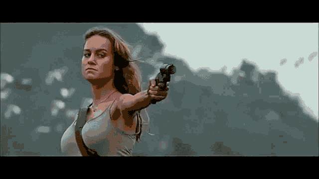 a woman is pointing a gun at the camera while standing in front of a mountain .