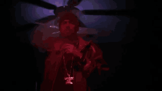 a man is holding a gun and wearing a necklace in a dark room .