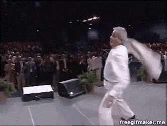 a man in a white suit is dancing on a stage in front of a crowd of people .