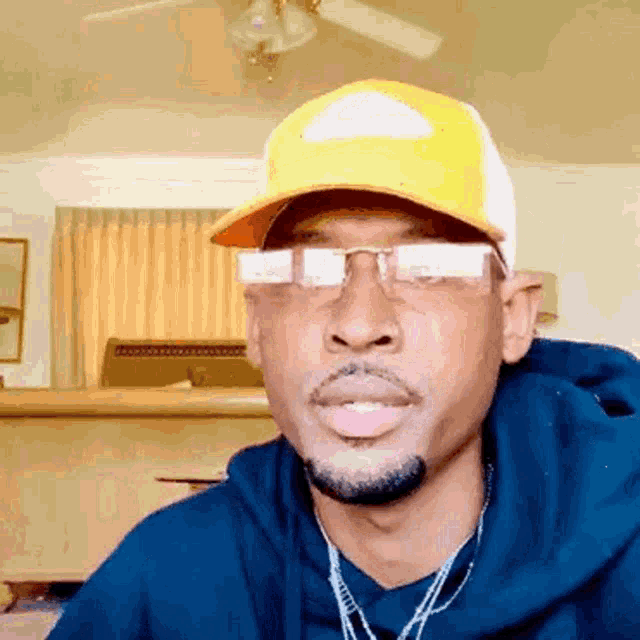 a man wearing a yellow hat and glasses is looking at the camera in a living room .