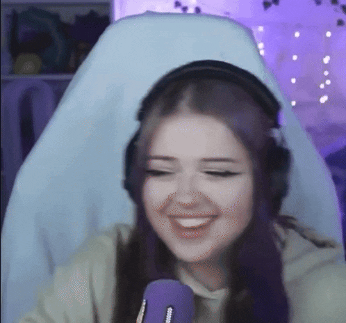 a girl with purple hair is wearing headphones and smiling while sitting in a chair in front of a microphone .