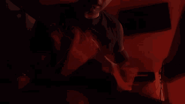 a man in a black shirt is standing in a dark room with a red light behind him