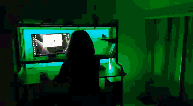 a woman sits at a desk in front of a computer with a blue light behind her