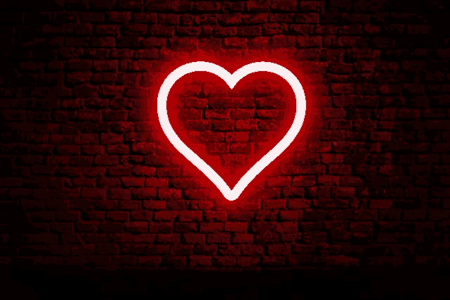 a red neon heart is glowing on a brick wall