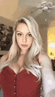 a woman in a red top is taking a selfie in a room with a ceiling fan in the background .