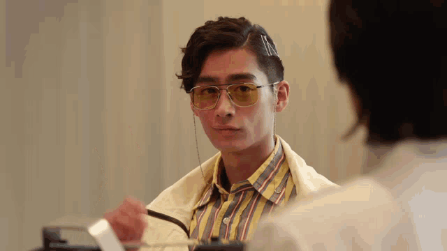 a man wearing sunglasses and a striped shirt looks at another man