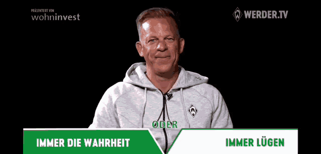 a man in a hoodie is on a television screen with the words immer die wahrheit written on it