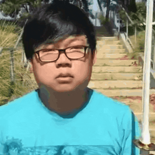 a young man wearing glasses and a blue shirt stands in front of stairs .