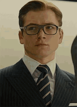 a man in a suit and tie is wearing glasses and making a funny face .