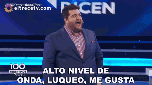 a man in a suit stands in front of a sign that says " alto nivel de onda luqueo me gusta "