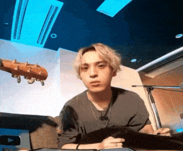 a young man sitting in front of a microphone with a guitar behind him