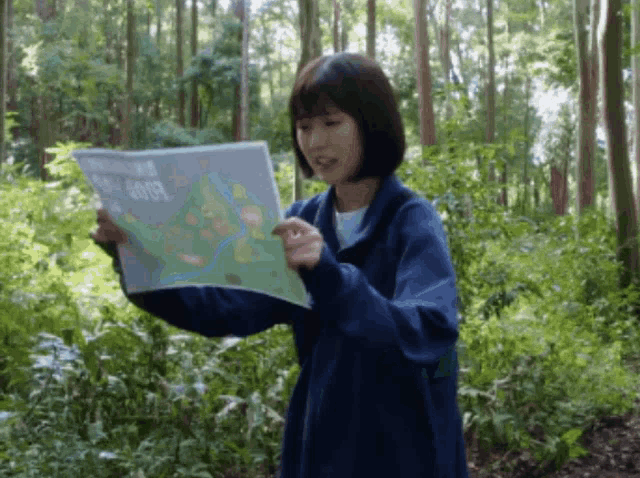 a woman in a blue jacket is holding a map in the woods that says good