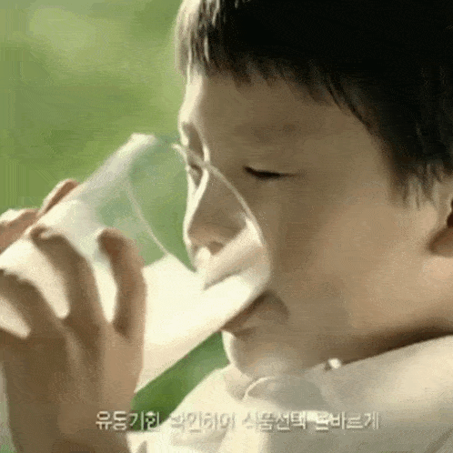 a young boy is drinking a glass of milk with foreign writing on the bottom