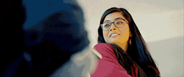 a woman wearing glasses and a pink shirt is smiling and looking at the camera .