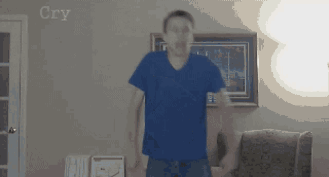 a man in a blue shirt is standing in a living room with the word cry written on the wall behind him