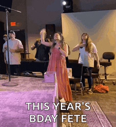 a woman in a pink dress stands in front of a microphone with the words this year 's bday fete