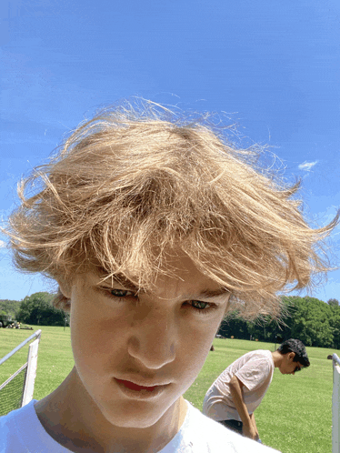 a boy with blonde hair looks at the camera with another boy in the background